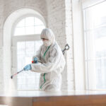 Coronavirus Pandemic. A disinfector in a protective suit and mask sprays disinfectants in the room. Protection of COVID-19 disease. Prevention of spreding pneumonia virus with surfaces we touch.