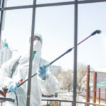 Coronavirus Pandemic. A disinfector in a protective suit and mask sprays disinfectants in the room. Protection of COVID-19 disease. Prevention of spreding pneumonia virus with surfaces we touch.